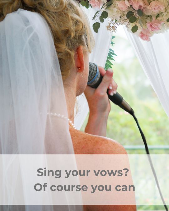 Blonde bride, wearing a veil attached to the
back of her head and a string of pearls, singing
into a corded microphone.