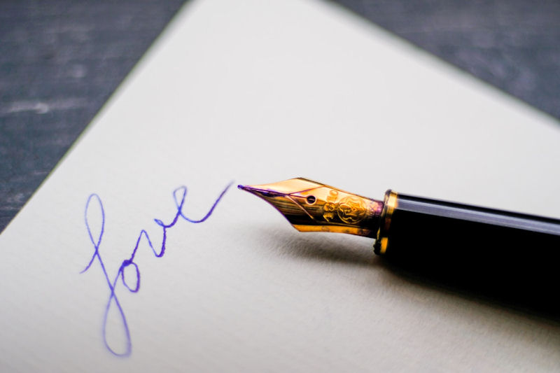 Black fountain pen lying on a sheet of
white paper on which the word Love has been
written in blue ink